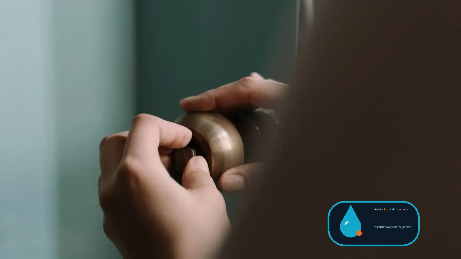 Hands checking a leaking pipe under a kitchen sink before residential water damage restoration