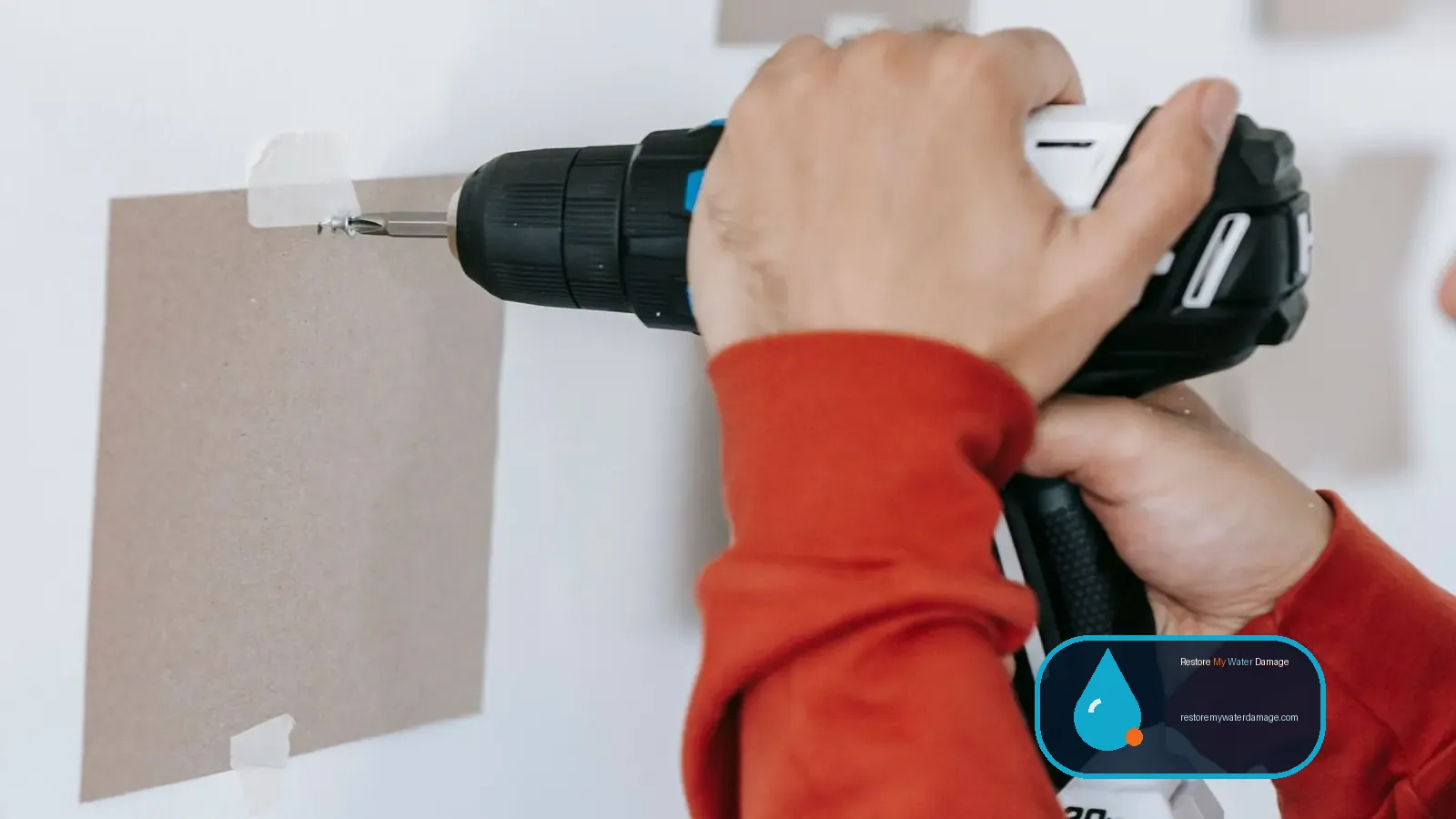 Hands drilling a hole in a wall, as done when setting up water damage restoration equipment